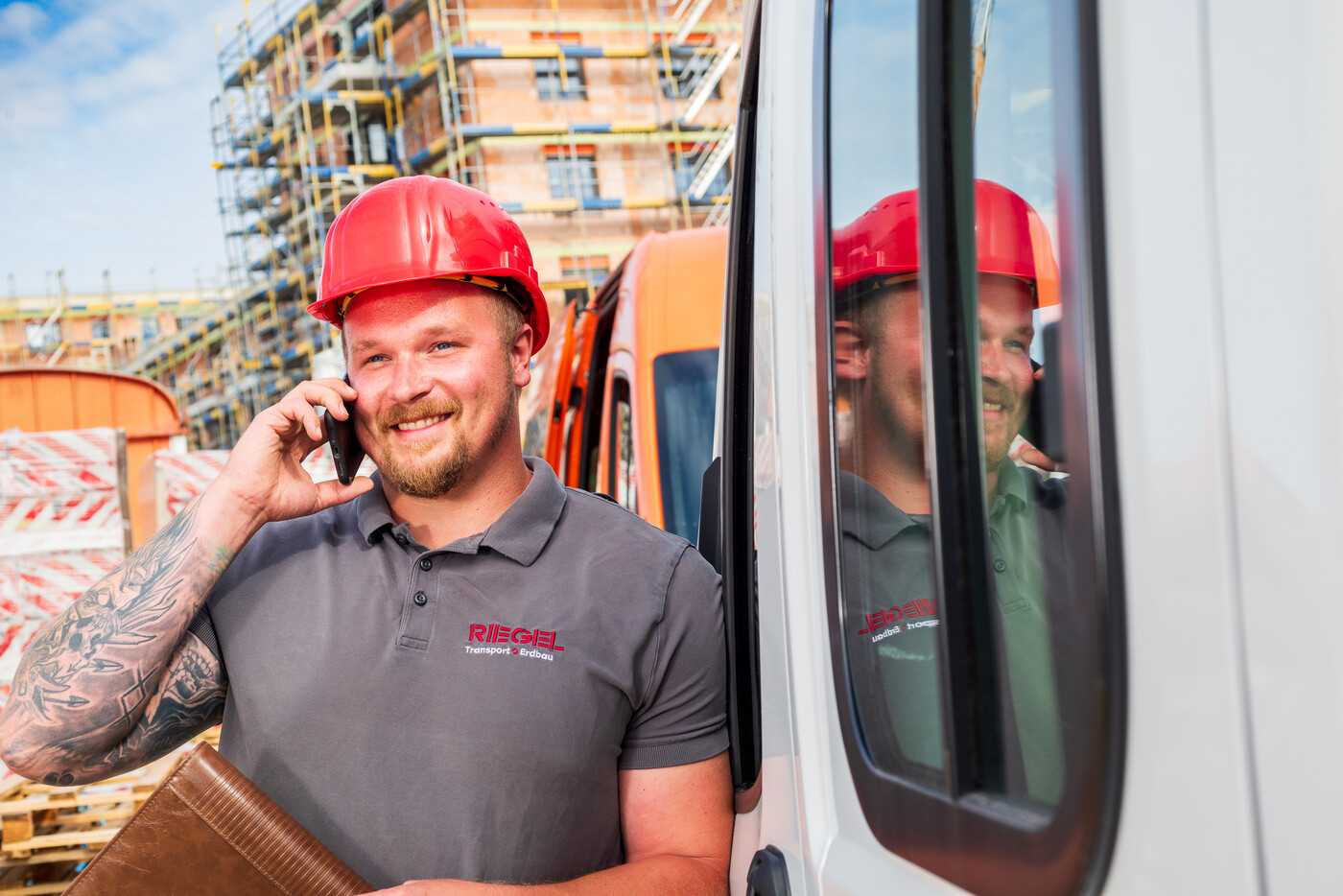 Bauleiter mit Helm telefoniert vor einem weißen Baustellenfahrzeug.